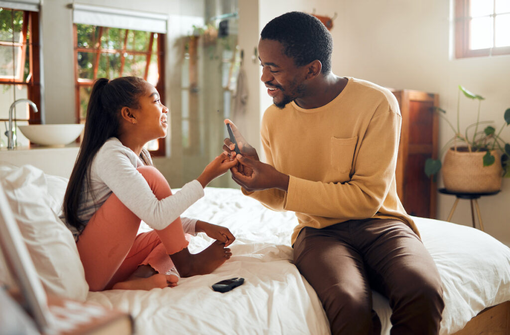 father and daughter in a bedroom, drawing blood for a glucose test to manage diabetes